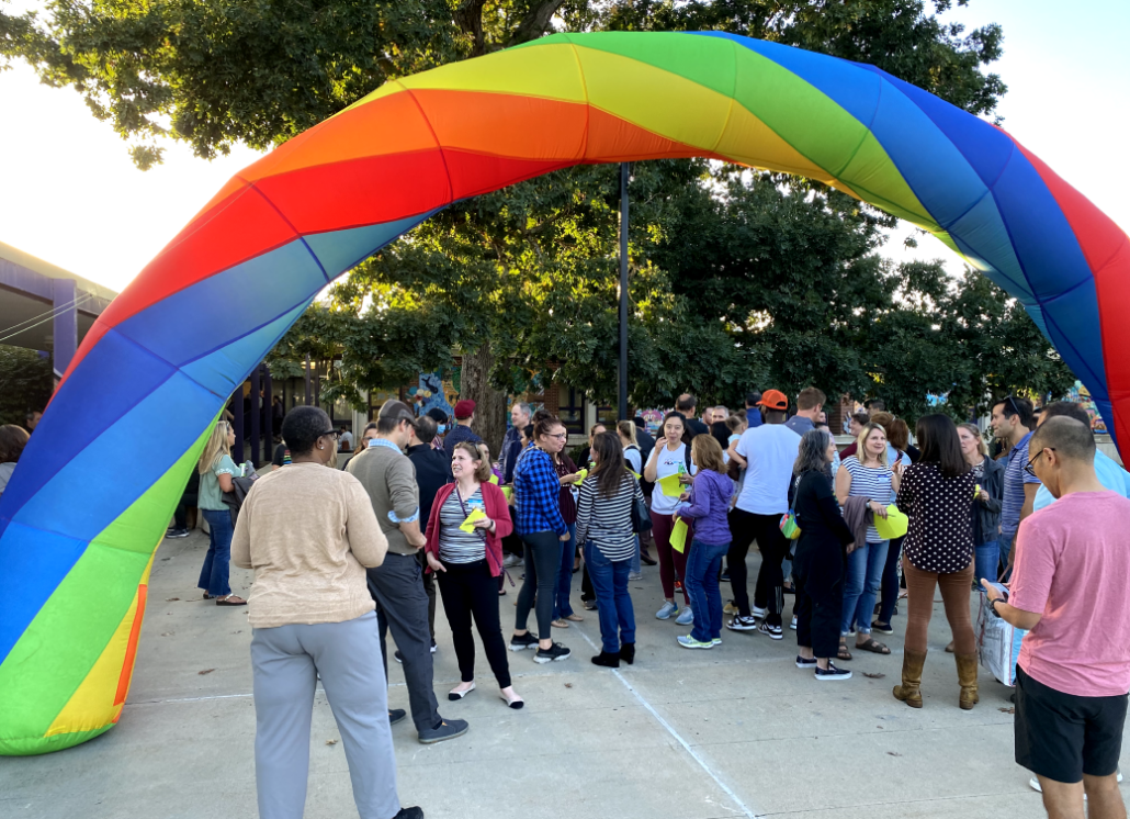 A crowd of people standing under a rainbow arch.